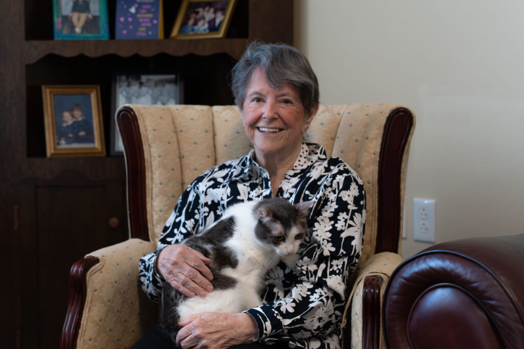 Resident smiling, sitting on a comfortable chair with her pet cat on her lap.