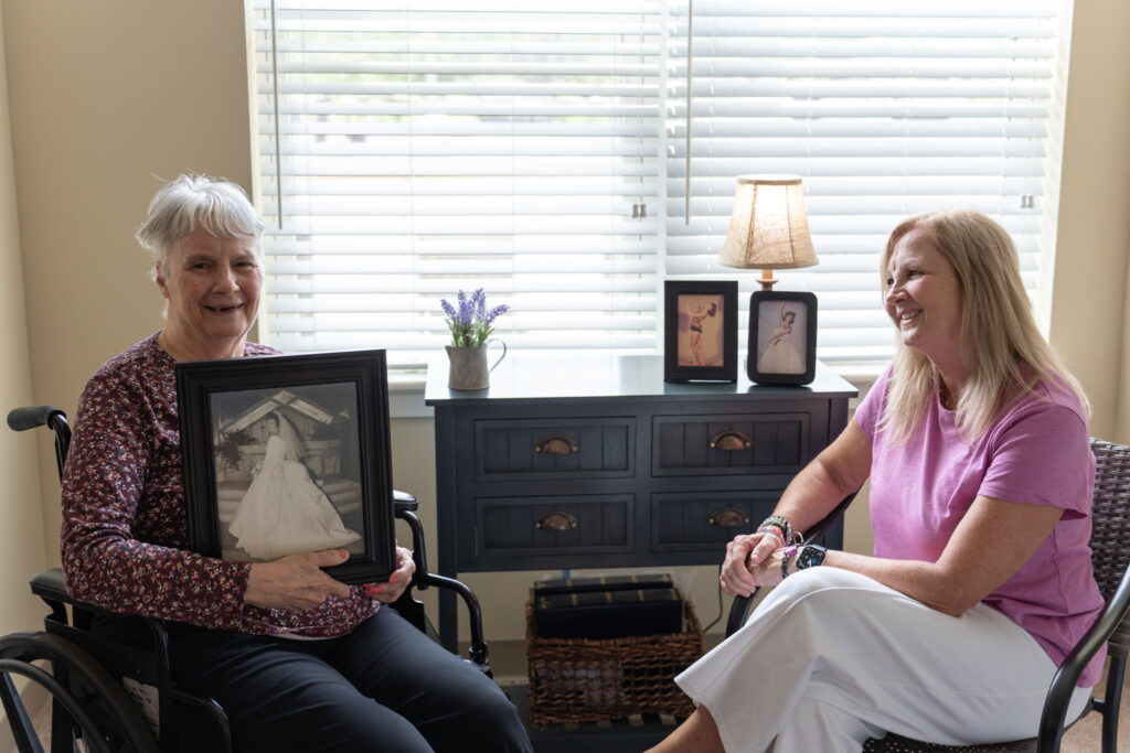 Senior woman sharing a framed wedding photo, highlighting connection, storytelling, and memory care support at Kingsland Walk.